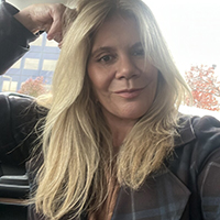 A woman, identified by the user as Jennifer Tisdale, sits inside a car with long blonde hair, looking at the camera with a slight smile. Autumn trees and a building are visible through the window behind her.