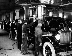Historic automotive assembly line with factory workers building early-model cars, showcasing the origins of modern vehicle manufacturing and industry innovation.