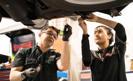 Tech trainer and student looking under a vehicle on a lift